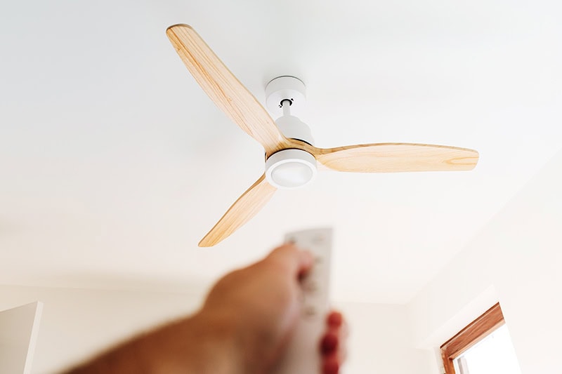 How to Choose the Right Ceiling Fan for Your Space. A person turning on a remote control ceiling fan.