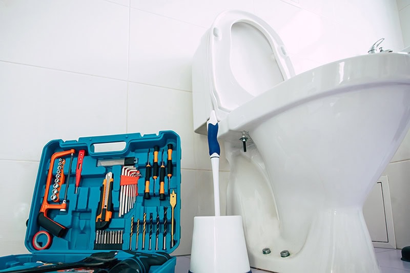 How to Unclog Your Slow-Draining Toilet in Springfield. Close up photo of ceramic bowl toilet in domestic bathroom with a box of tools.